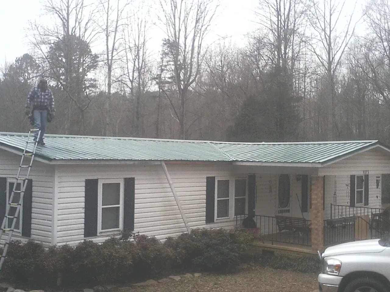 Worker on a ladder beside a new green metal roof on a ranch home in Flint