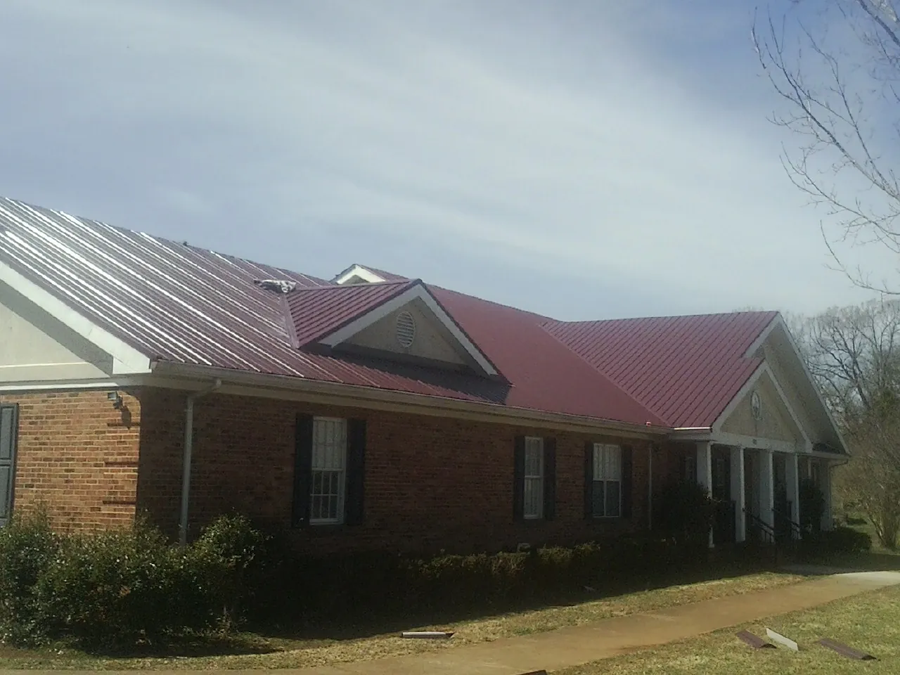 Red metal roof with gabled entries on a long brick building, from a Hail Damage Roof Repair job in Flint