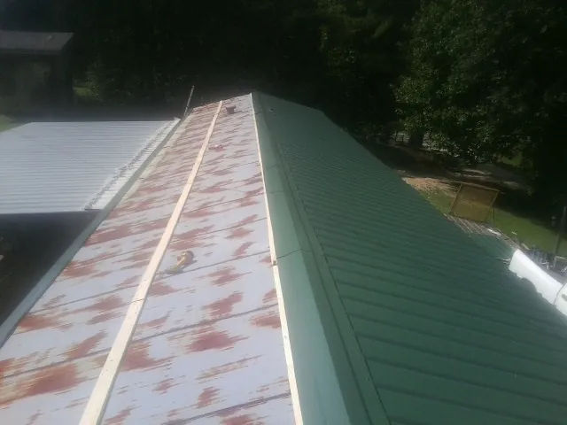 Old rusted panels beside newly installed green metal roofing — Wind Damage Roof Repair by Roofing Brothers in Flint