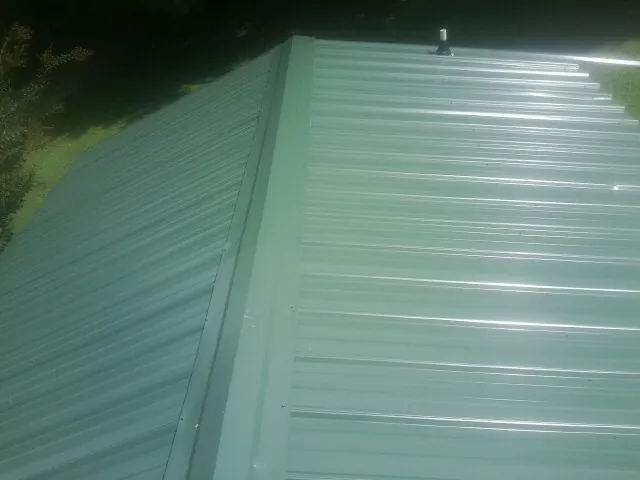 New green metal panels meeting at the ridge of a roof — Flat Roof Repair work by our crew in Flint