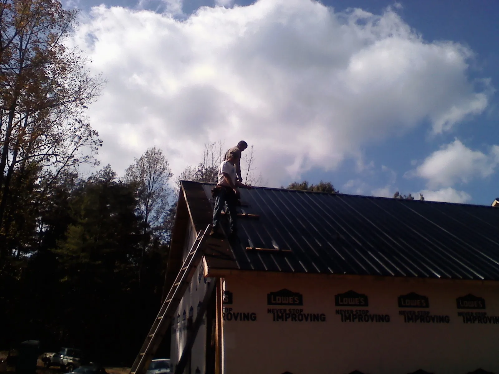Roofer fastening dark metal panels high against a cloudy sky, from a Roof Inspection job in Flint