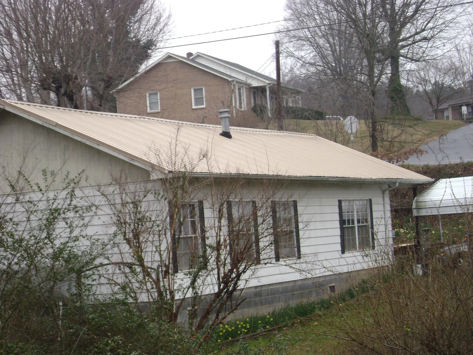 Tan metal roof on a white sided house set into a hillside — Commercial Roofing by Roofing Brothers in Flint