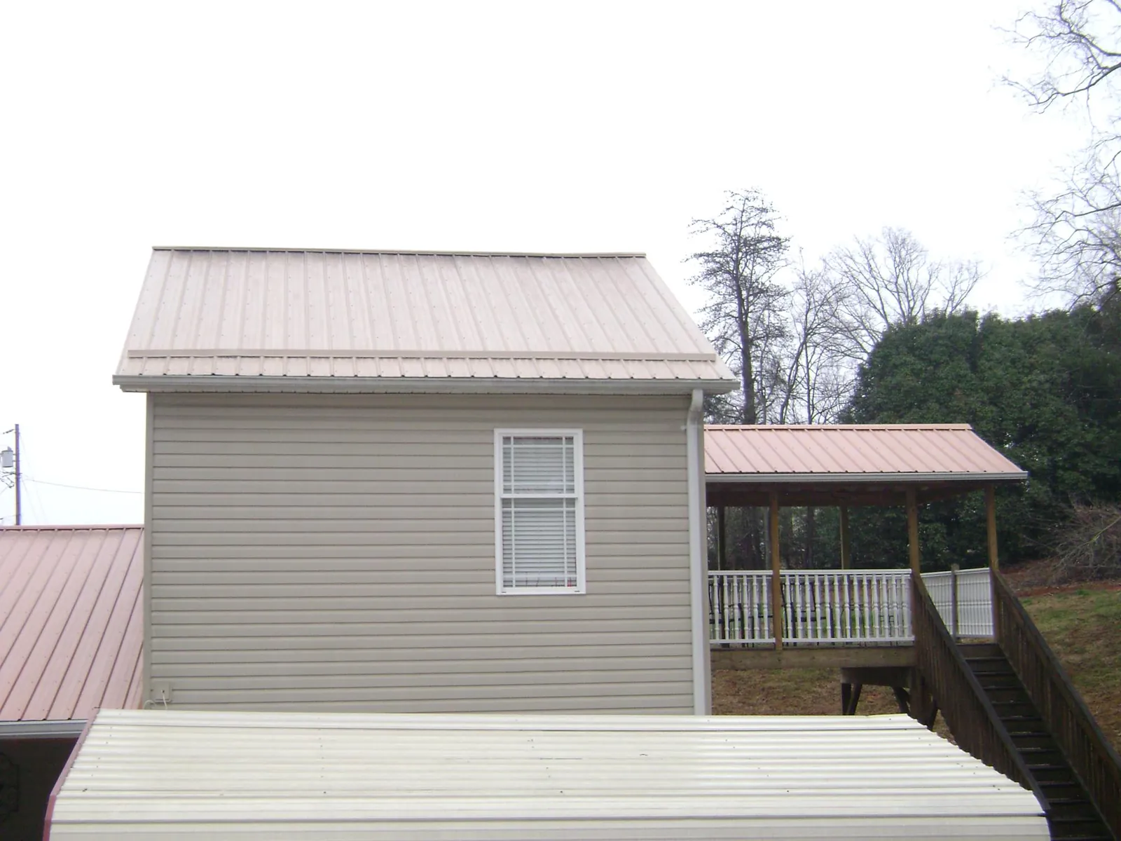 Tan metal roofs on a two story addition and attached porch, from a Roof Replacement job in Flint